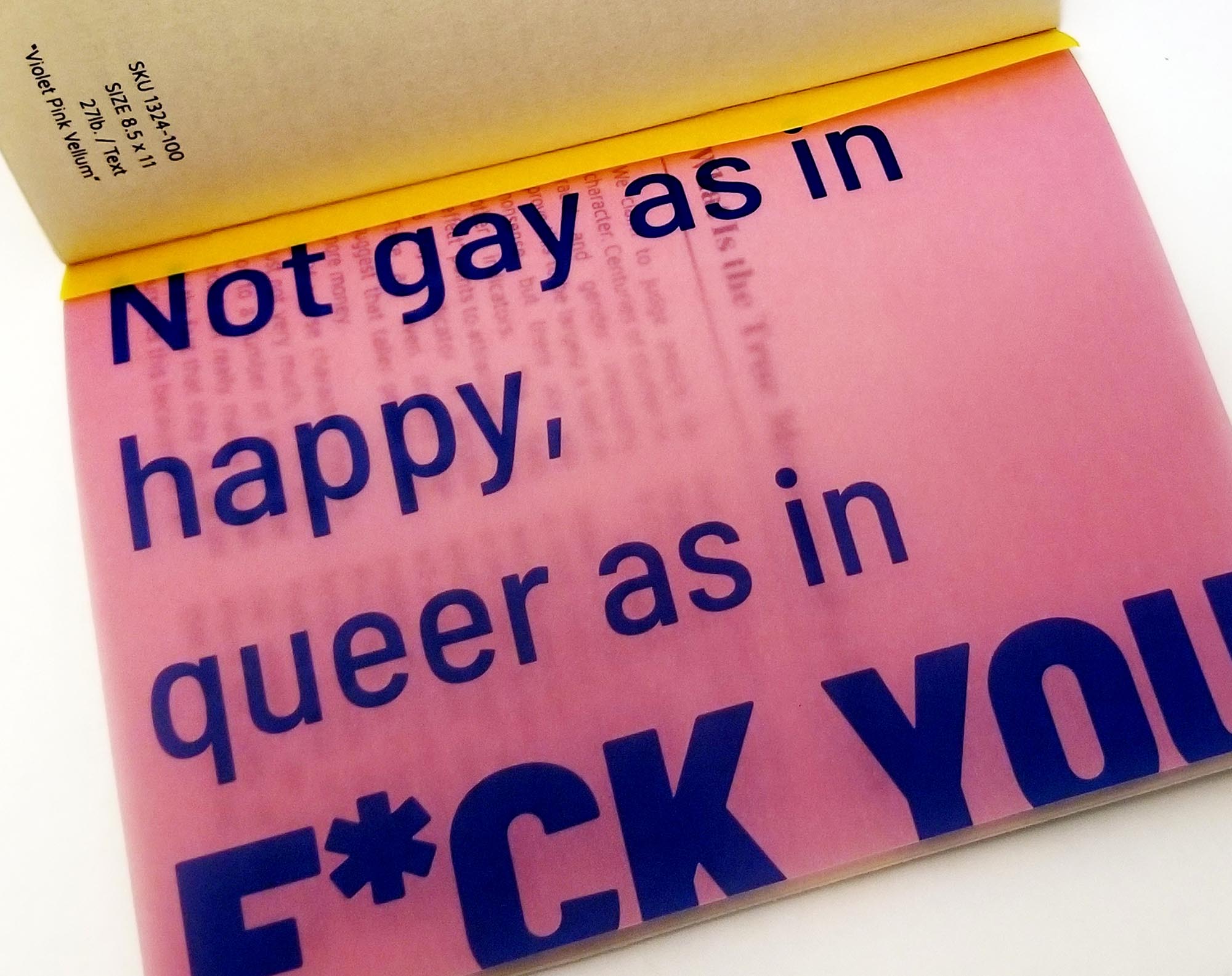 close up view of pink transparent paper with blue text that reads “Not gay as in Happy, queer as in F*CK YOU”